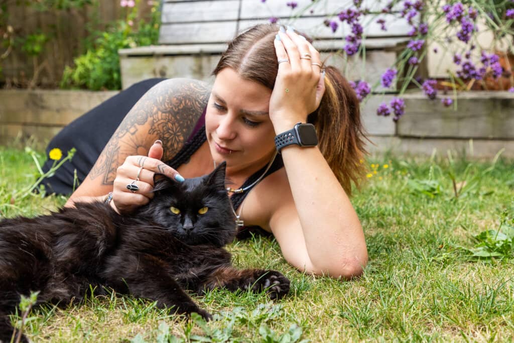 A long-haired black cat and their owner laying down in a garden.
