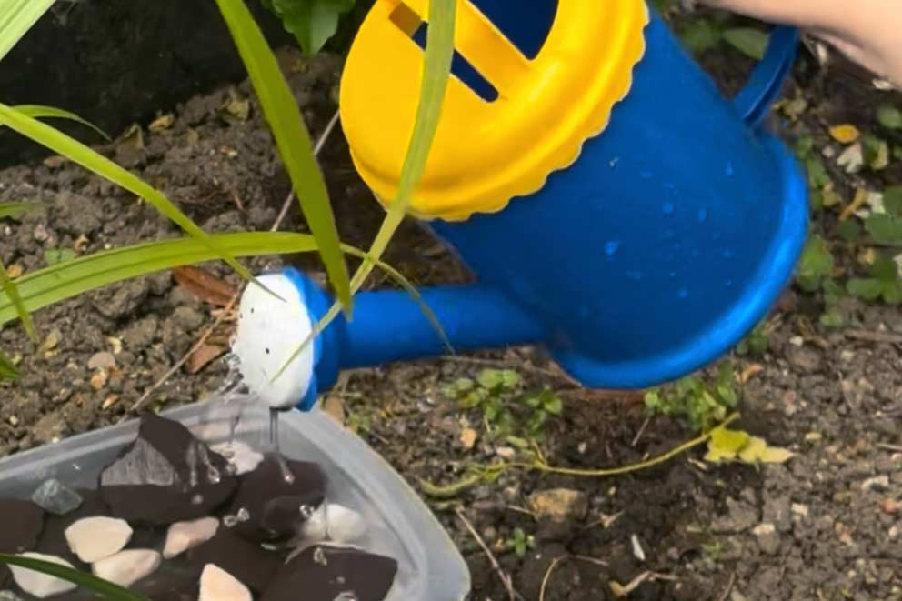Water from a blue and yellow watering can filling up the new water station.