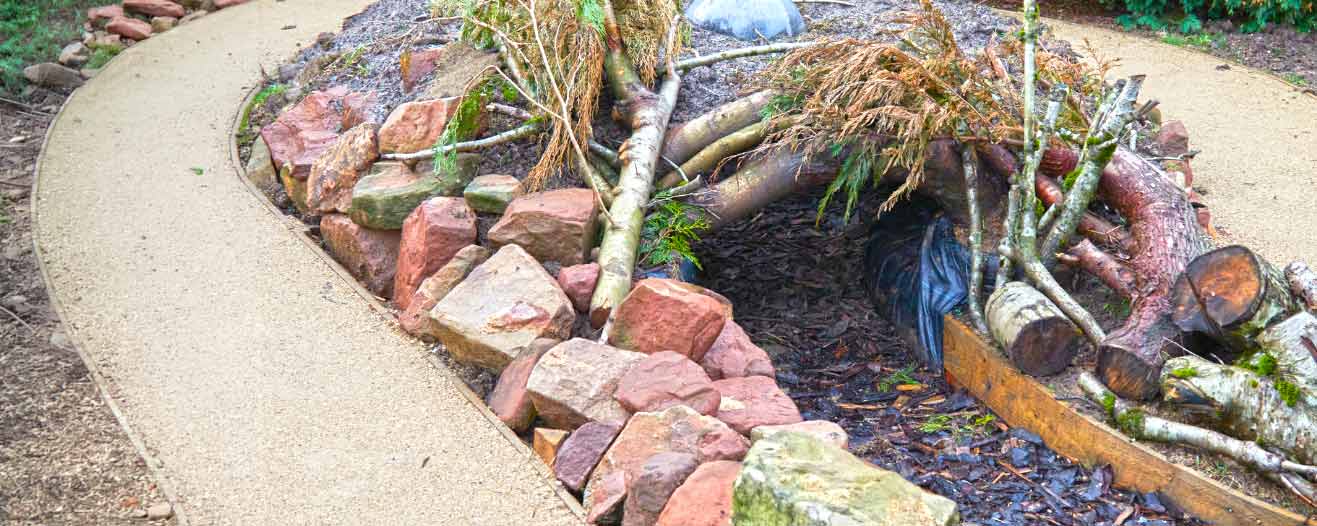 A constructed animal den made from rocks and branches sits next to a curved gravel path.